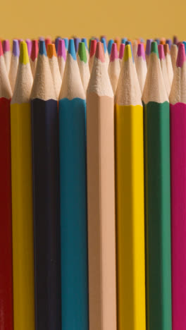 Vertical-Video-Studio-Shot-Of-Rotating-Multi-Coloured-Pencils-Against-Yellow-Background-1